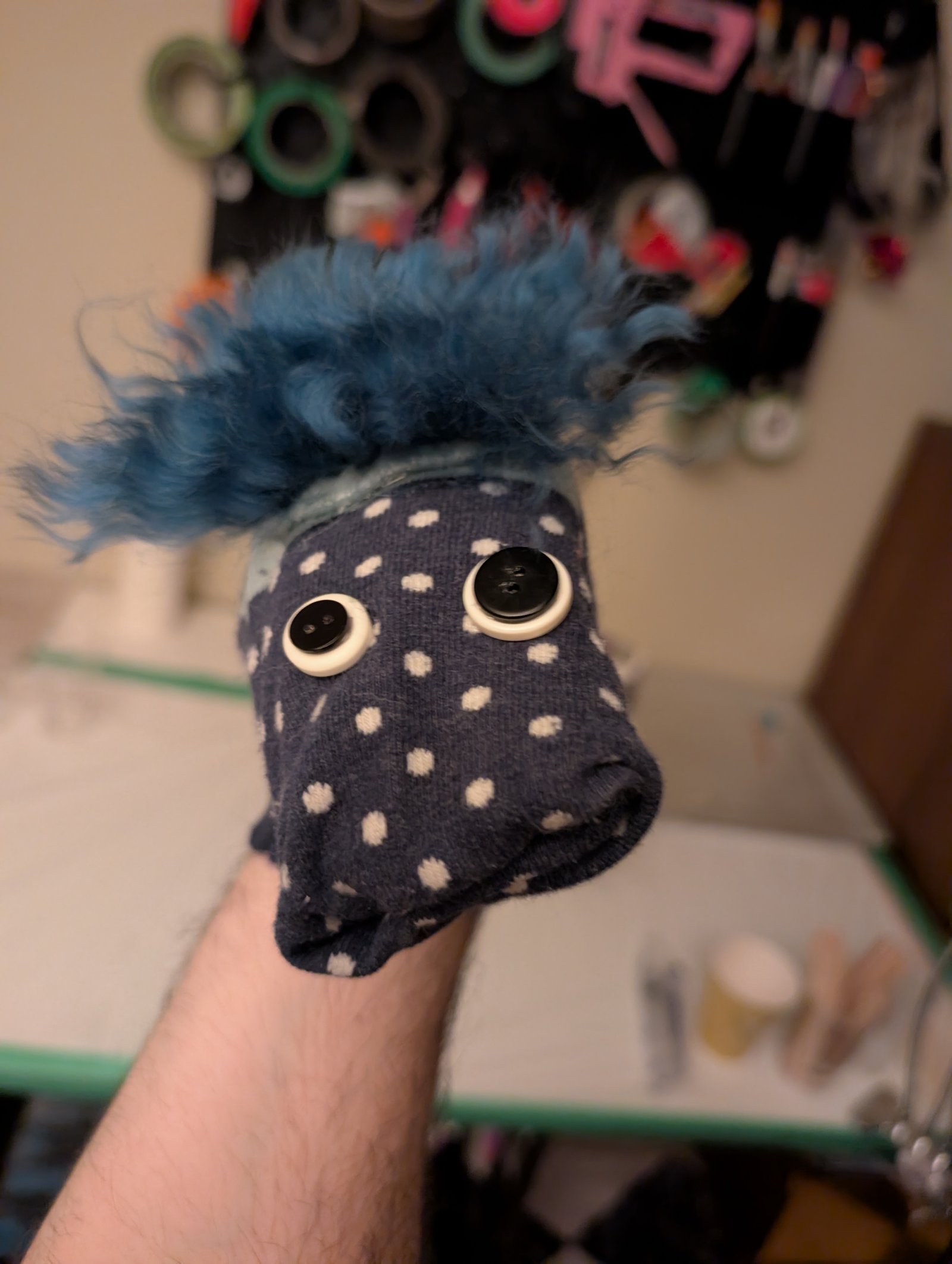 A blue sock puppet with muppet-style hair and button eyes